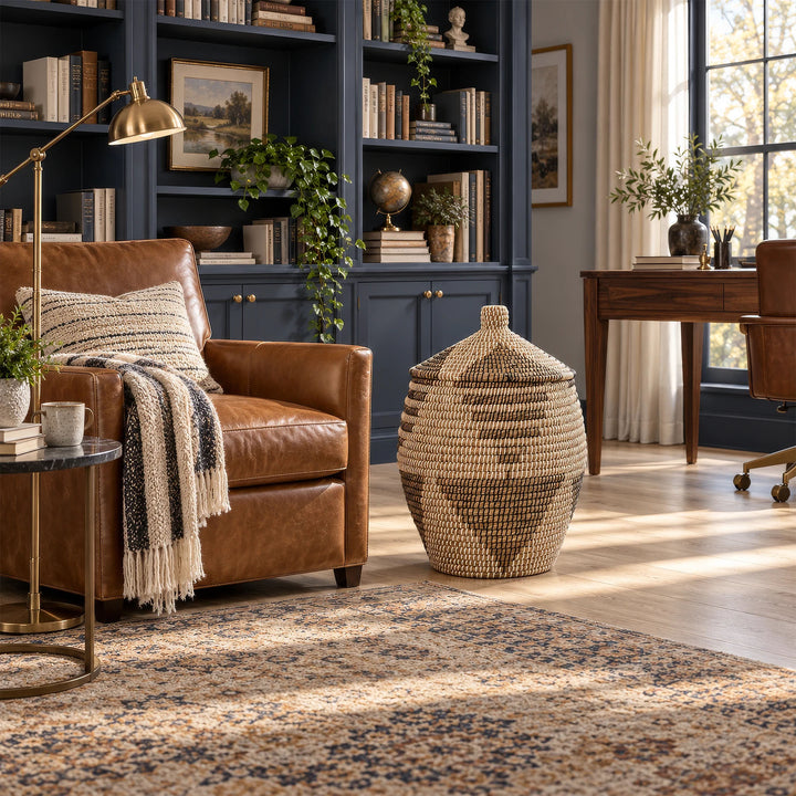 Καλάθι θαλασσόχορτου με μοτίβο, κλειστό κωνικό καπάκι δίπλα σε καφέ δερμάτινη πολυθρόνα σε χώρο με βιβλιοθήκες.